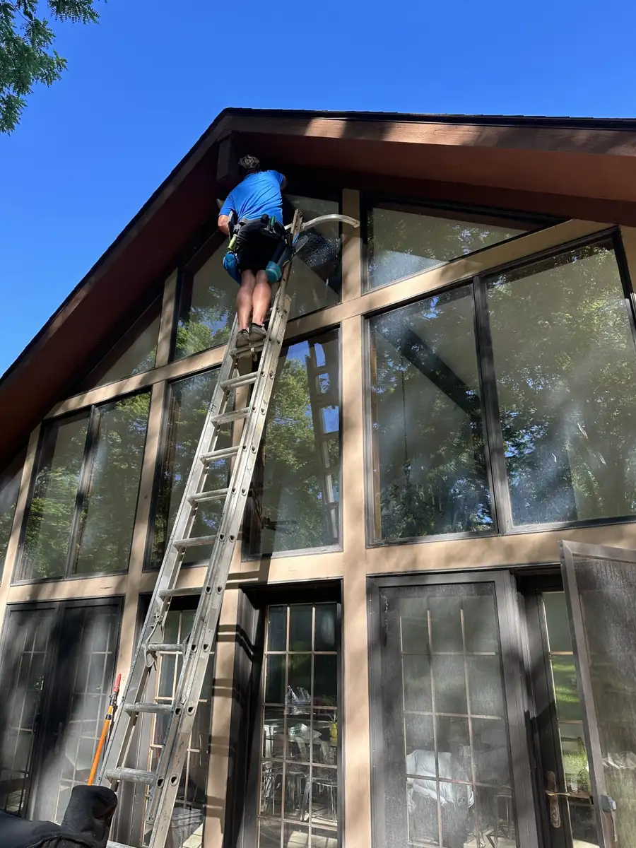 Skyline technician cleaning tall gable windows from a ladder